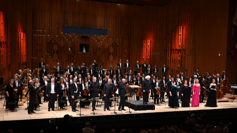 The cast of Katya Kabanova with the London Symphony Orchestra, on stage at the Barbican Hall,following the concert performance on 11 January 2023. At the front of the stage, from left to right: William Spaulding (chorus director), Lukáš Zeman (Kuligin), Andrew Staples (Tichon), Simon O’Neill (Boris), Ladislav Elgr (Kudryash), Pavlo Hunka (Dikoy), Sir Simon Rattle  (conductor), Claire Barnett-Jones Glasha (Feklusha), Katarina Dalayman (Kabanicha), Magdalena Kožená (Varvara), and Amanda Majeski (Katya). (credit: Mark Allan) 