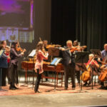 A note-worthy debut: Greg Murphy (center), a board member who doesn’t play violin, gets a quick lesson to help the Spartanburg Philharmonic musicians with Purcell’s ‘Fantasia Upon One Note.’ Facing him is concertmaster Joanna Mulfinger, who led the orchestra. (courtesy of Spartanburg Philharmonic)