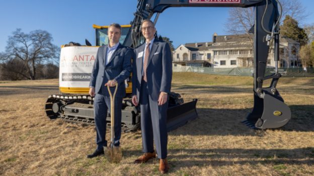 The Atlanta Opera's Tomer Zvulun and John Haupert pose in front of an excavator, with the historic Bobby Jones Golf Club in the background. (courtesy of The Atlanta Opera)
